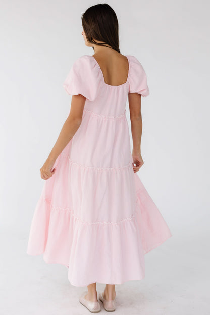 Back view of a woman wearing a pink gingham tiered midi dress with a square back neckline and balloon sleeves.