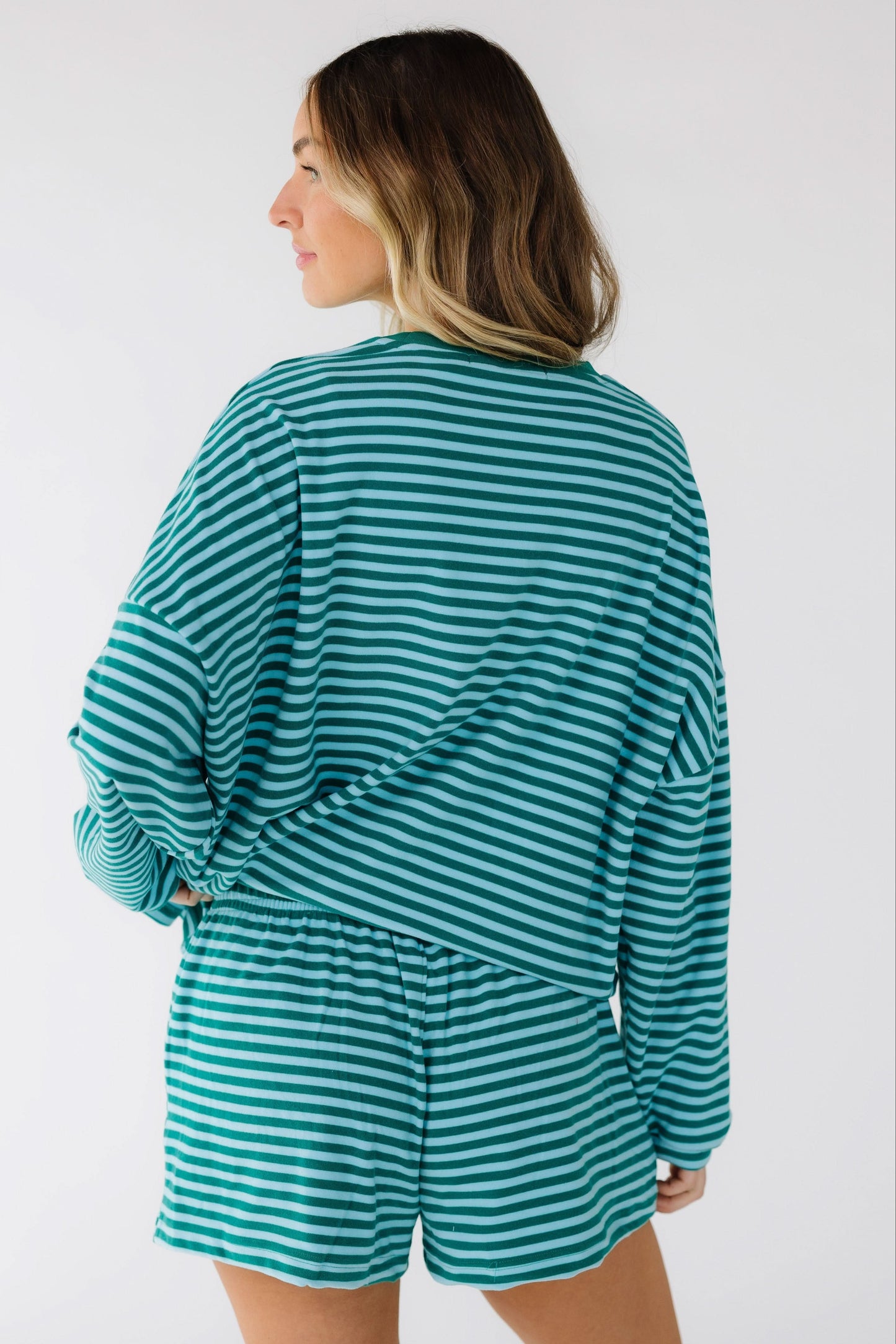 Back view of a woman wearing a loose fitting stripe shorts set in green & blue.