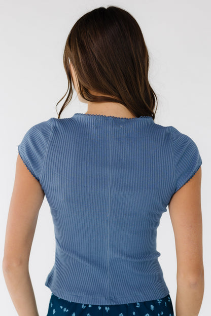 Back view of a woman wearing a rib knit close fitting blue top with cap sleeves.