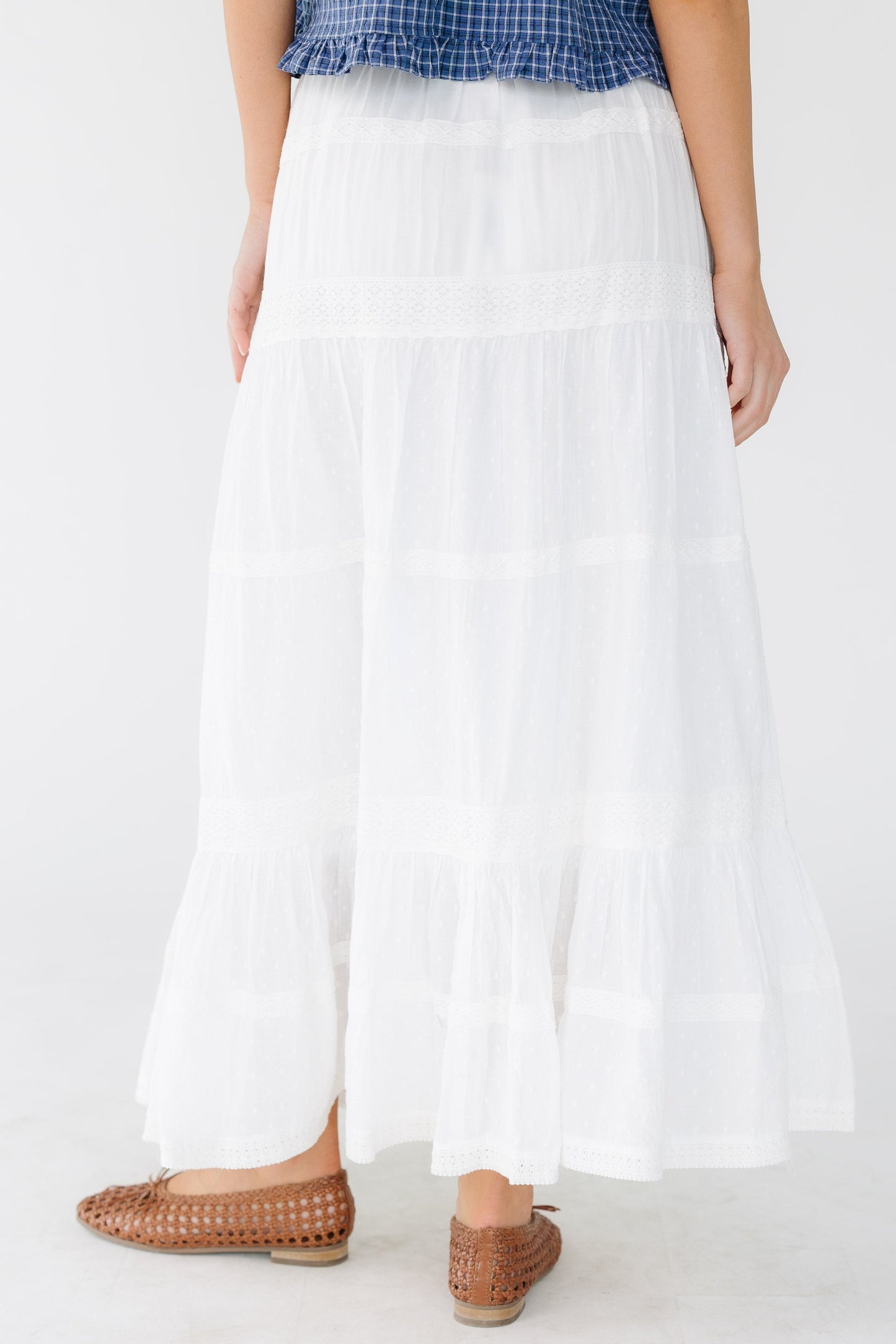 Back view of a woman wearing a white tiered and and lace trimmed midi skirt with an elastic waist.