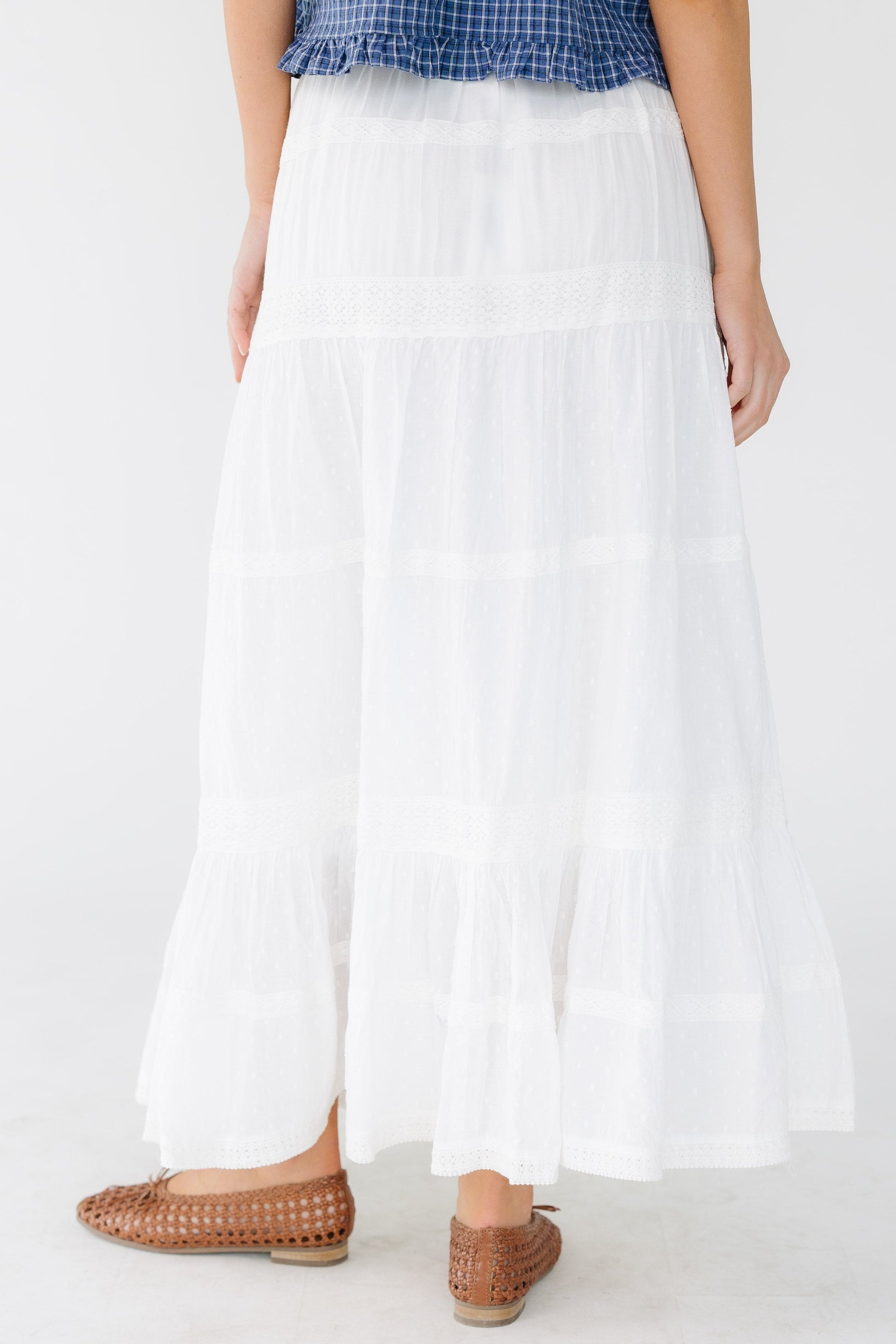 Back view of a woman wearing a white tiered and and lace trimmed midi skirt with an elastic waist.