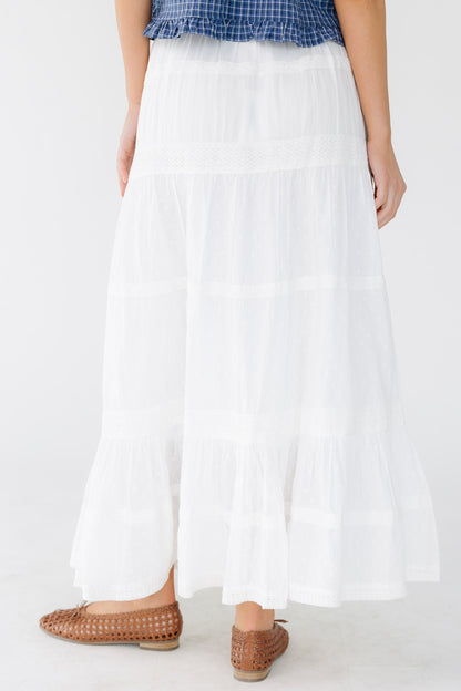 Back view of a woman wearing a white tiered and and lace trimmed midi skirt with an elastic waist.