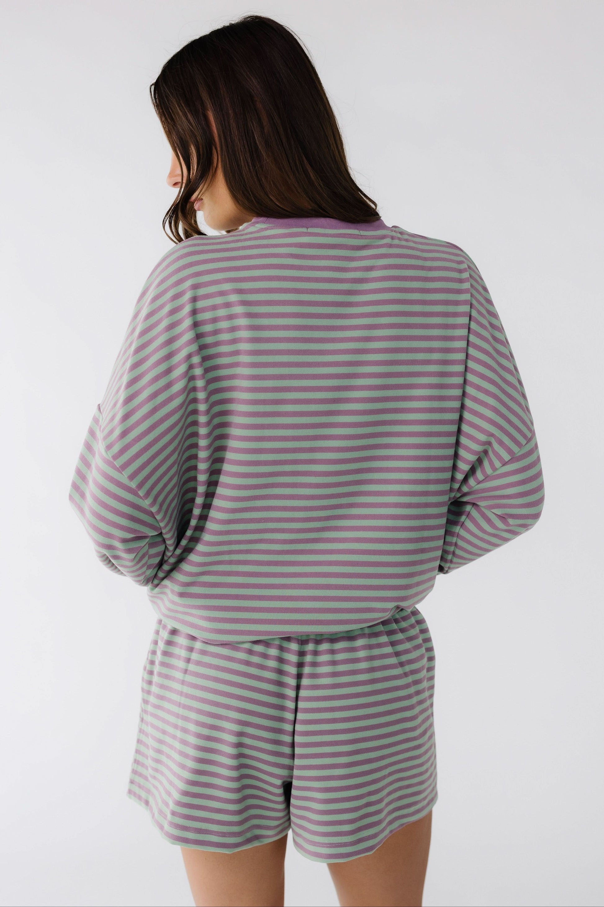 Back view of a woman wearing a purple & green stripe shorts set with long sleeves.
