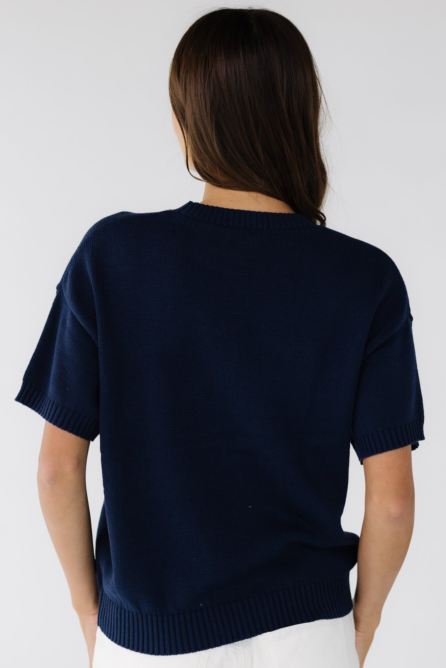 Back view of a young woman wearing a navy short sleeve sweater.