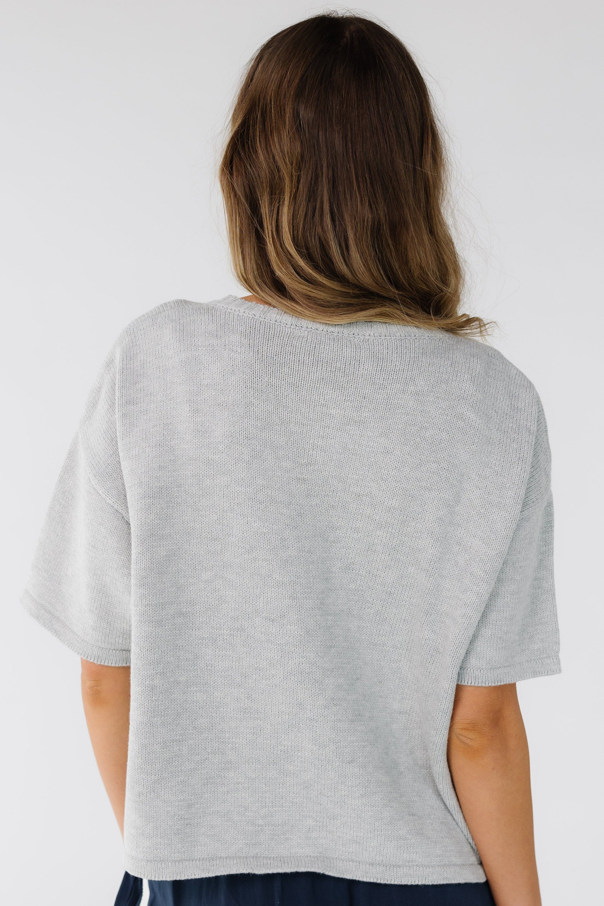 Back view of a woman wearing a grey loose fitting sweater with short sleeves.
