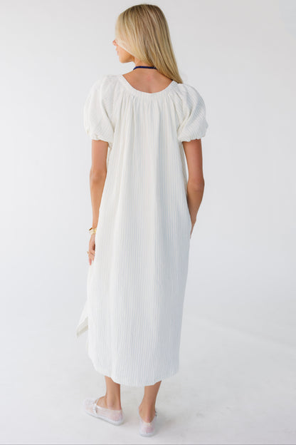 Back view of a woman wearing a white & blue stripe midi-maxi dress with a scoop neckline and balloon sleeves.
