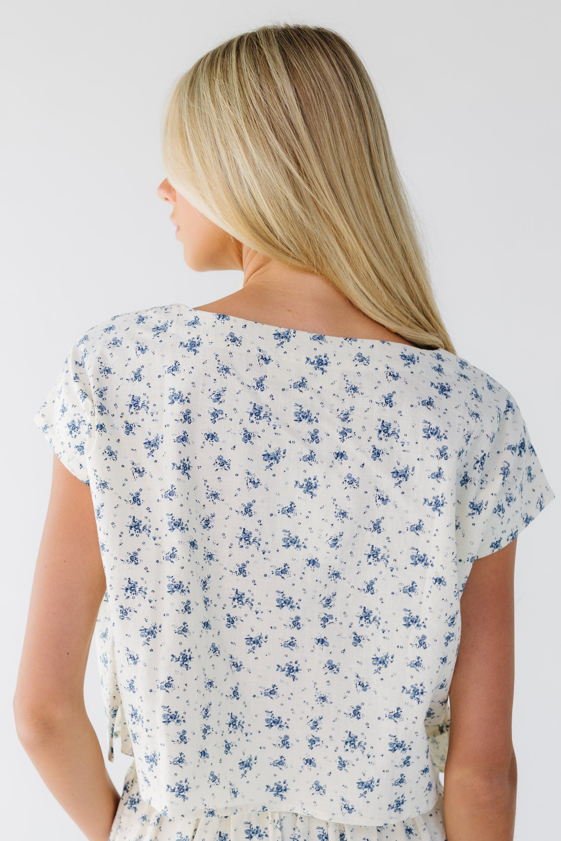 Back view of a woman wearing a cream with blue floral print top.