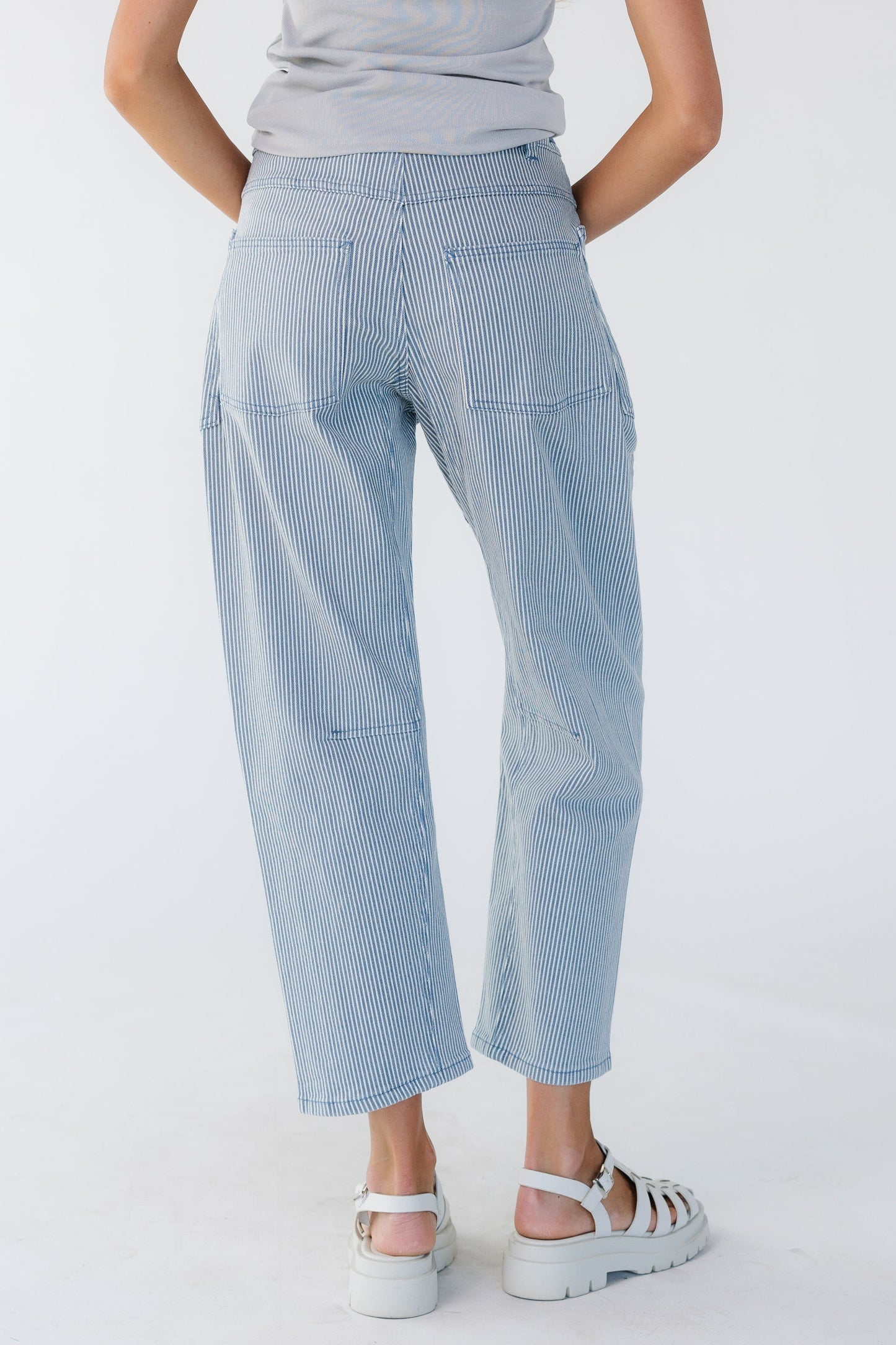 Back view of a young woman wearing blue & white stripe barrel jeans with back pockets.