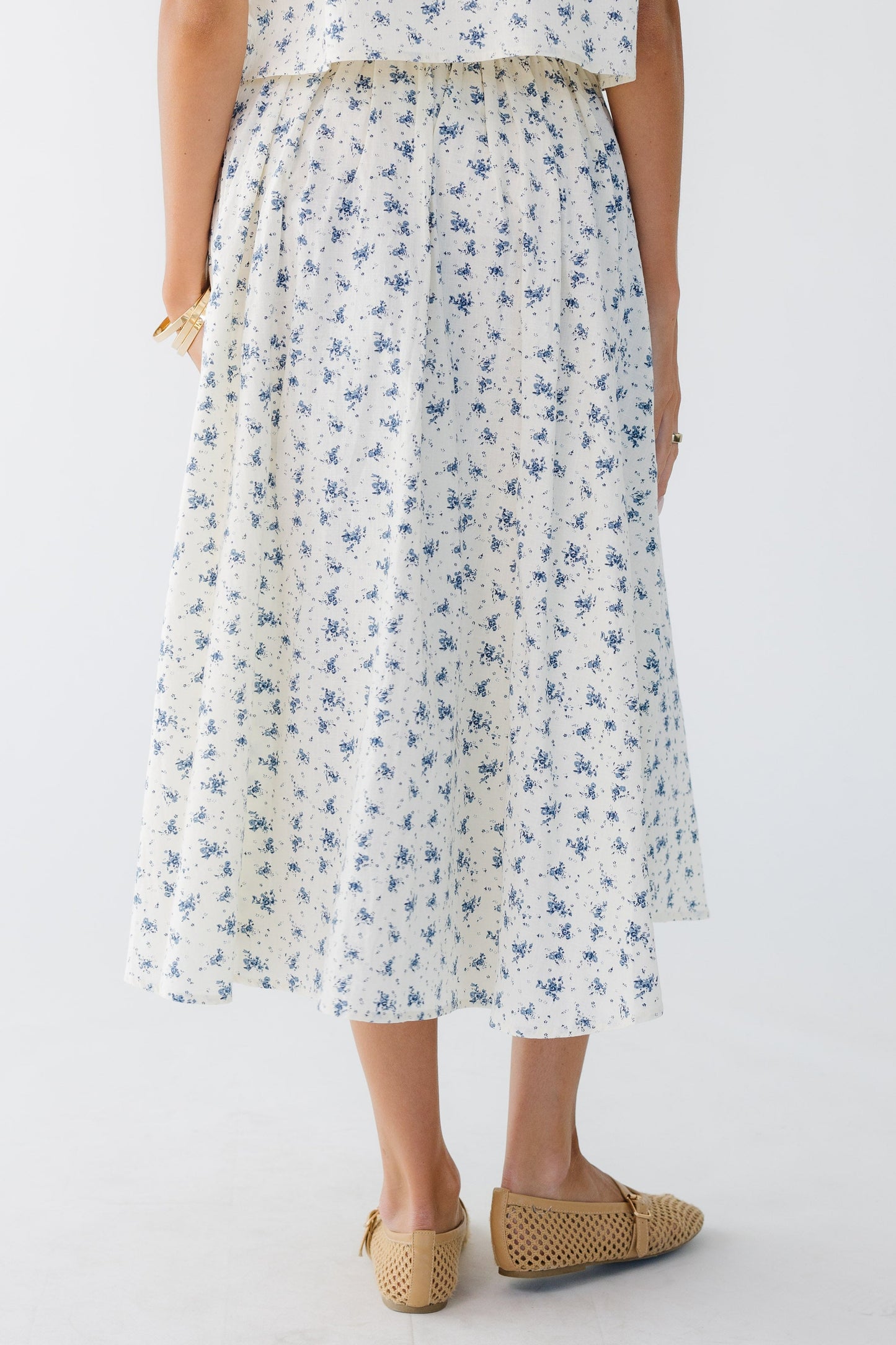 Back view of a woman wearing a cream and blue print midi skirt.