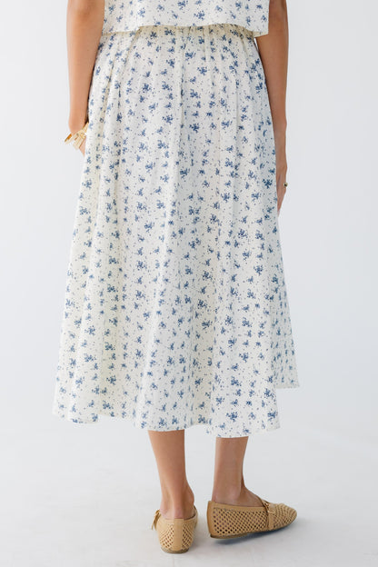 Back view of a woman wearing a cream and blue print midi skirt.