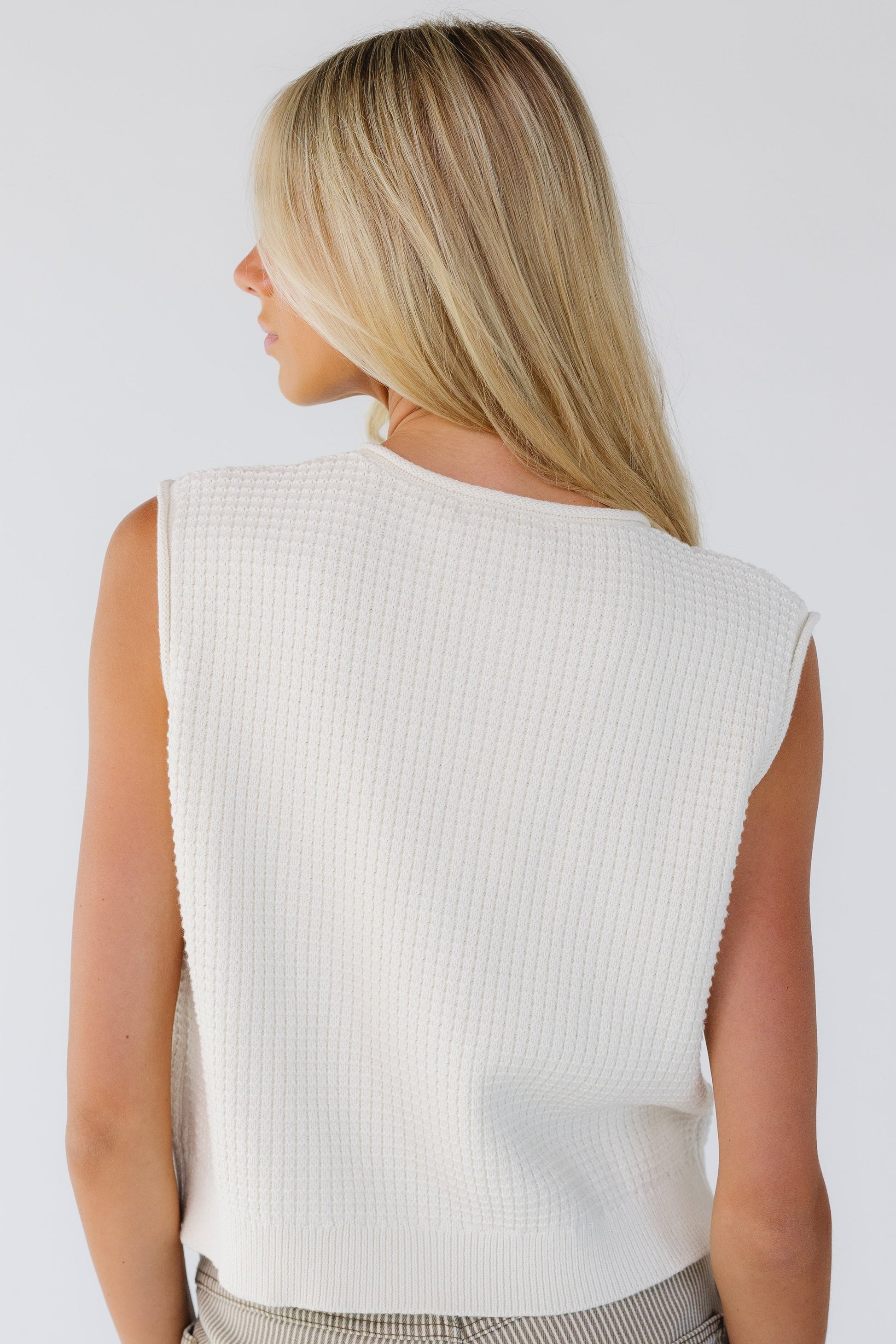 Back view of a woman wearing a cream textured sweater vest.