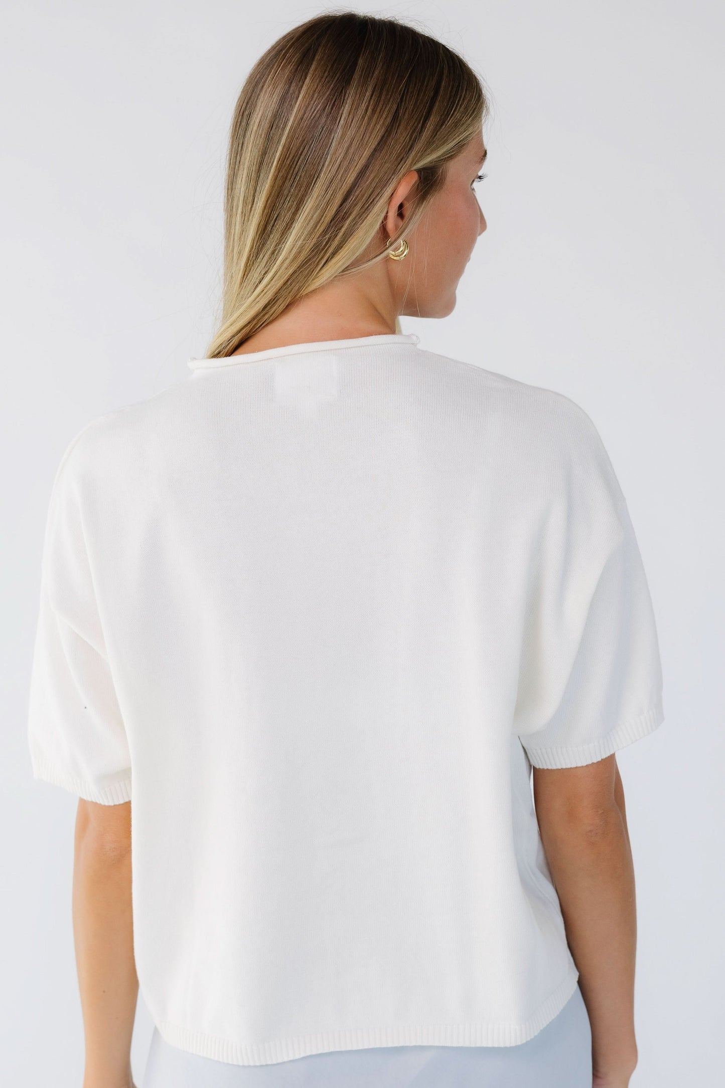 Back view of a woman wearing an ivory loose fitting cardigan with short sleeves.