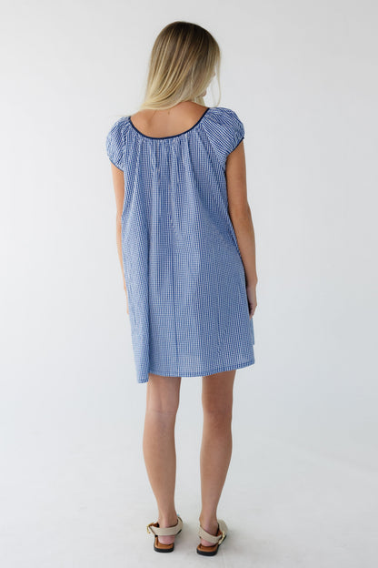 Back view of a woman wearing a navy gingham short dress with short sleeves and a wide scoop neckline.