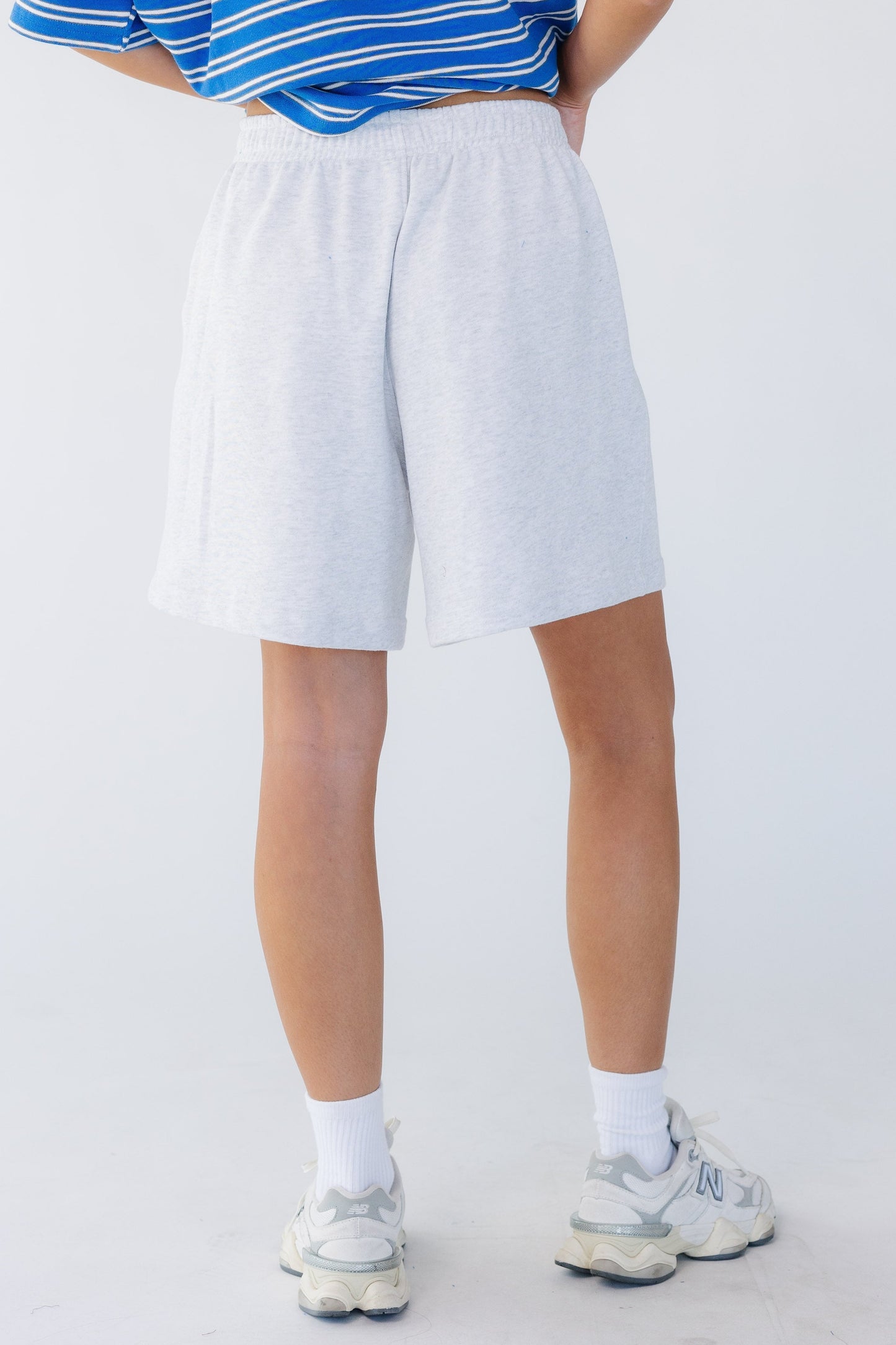Back view of a young woman wearing a pair of wide leg, loose fitting knit shorts with a wide elastic waistband.