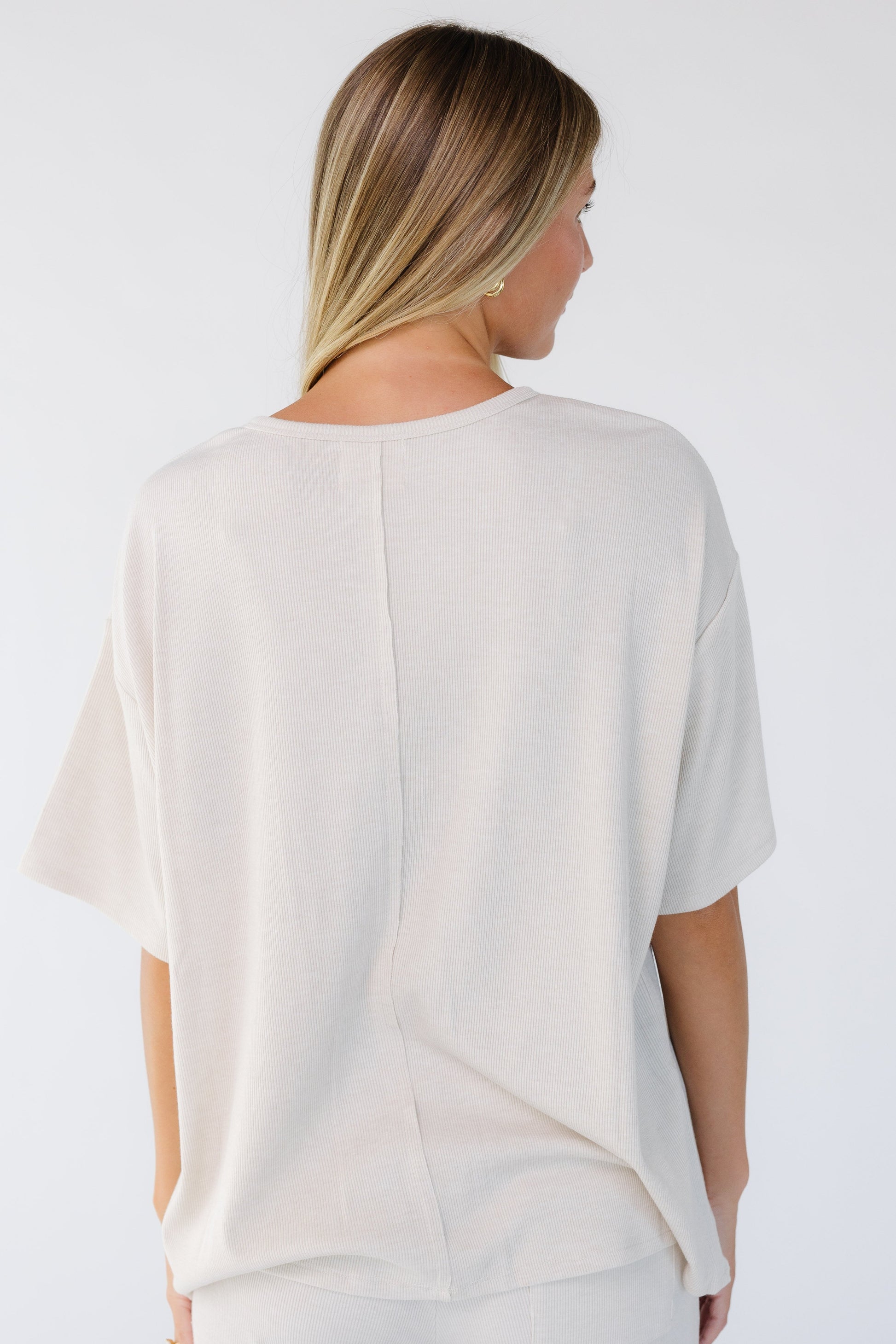 Back view of a woman wearing a beige loose fitting top with short sleeves and a round neckline.