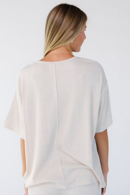 Back view of a woman wearing a beige loose fitting top with short sleeves and a round neckline.