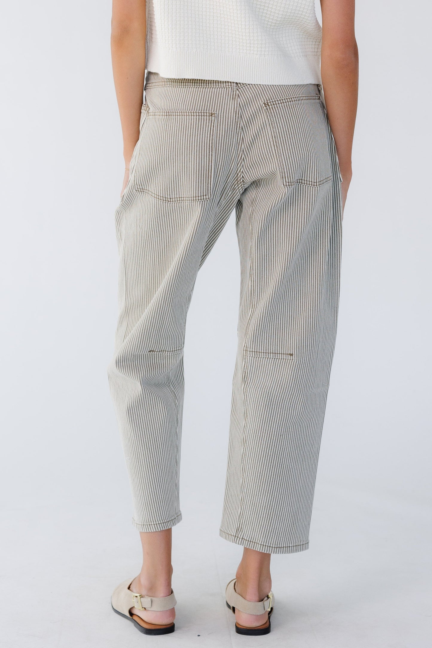 Back view of a woman wearing olive green and white stripe barrel jeans with 2 large back pockets.
