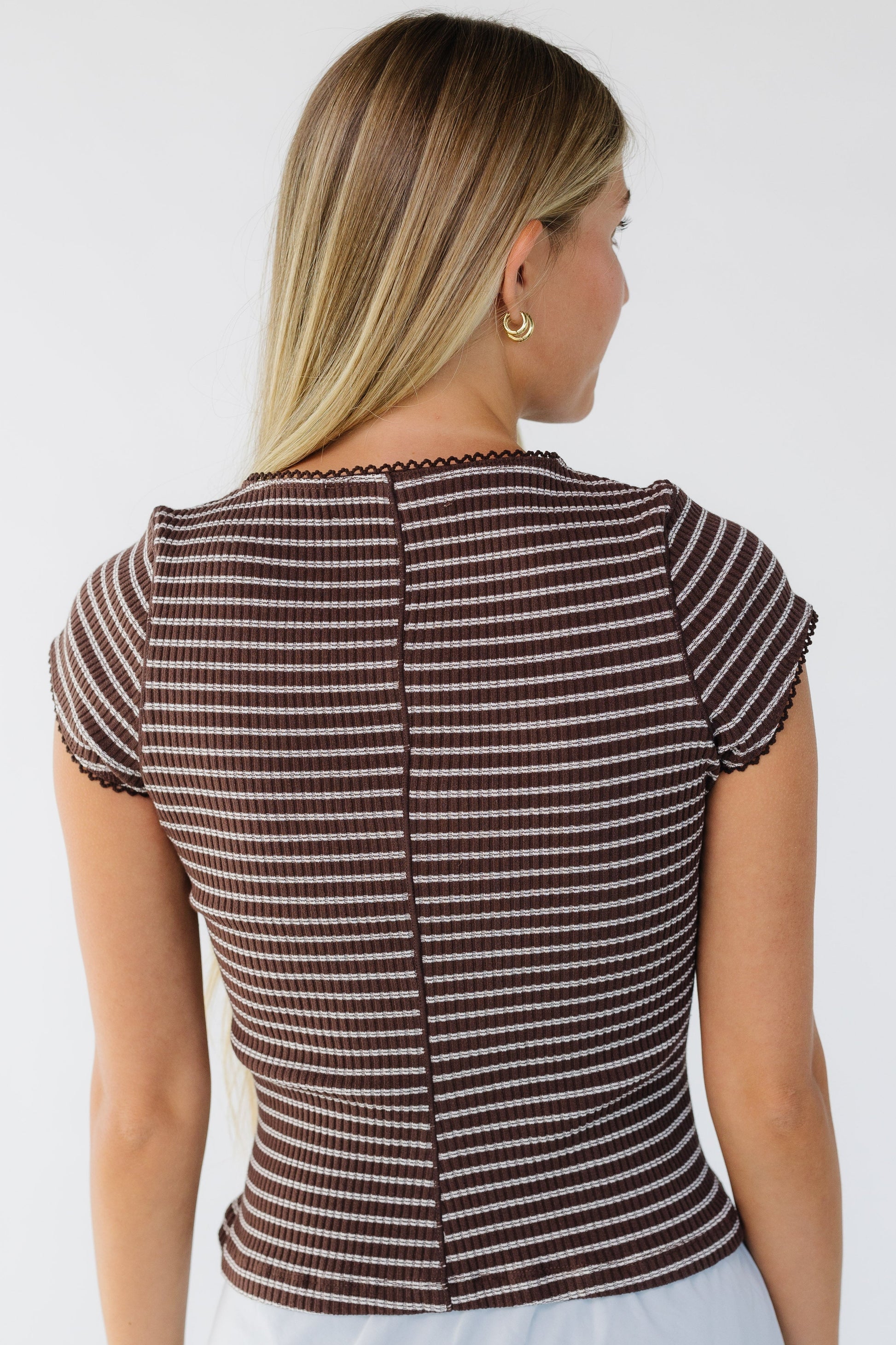 Back view of a woman wearing a brown & white stripe close fitting top with short sleeves.