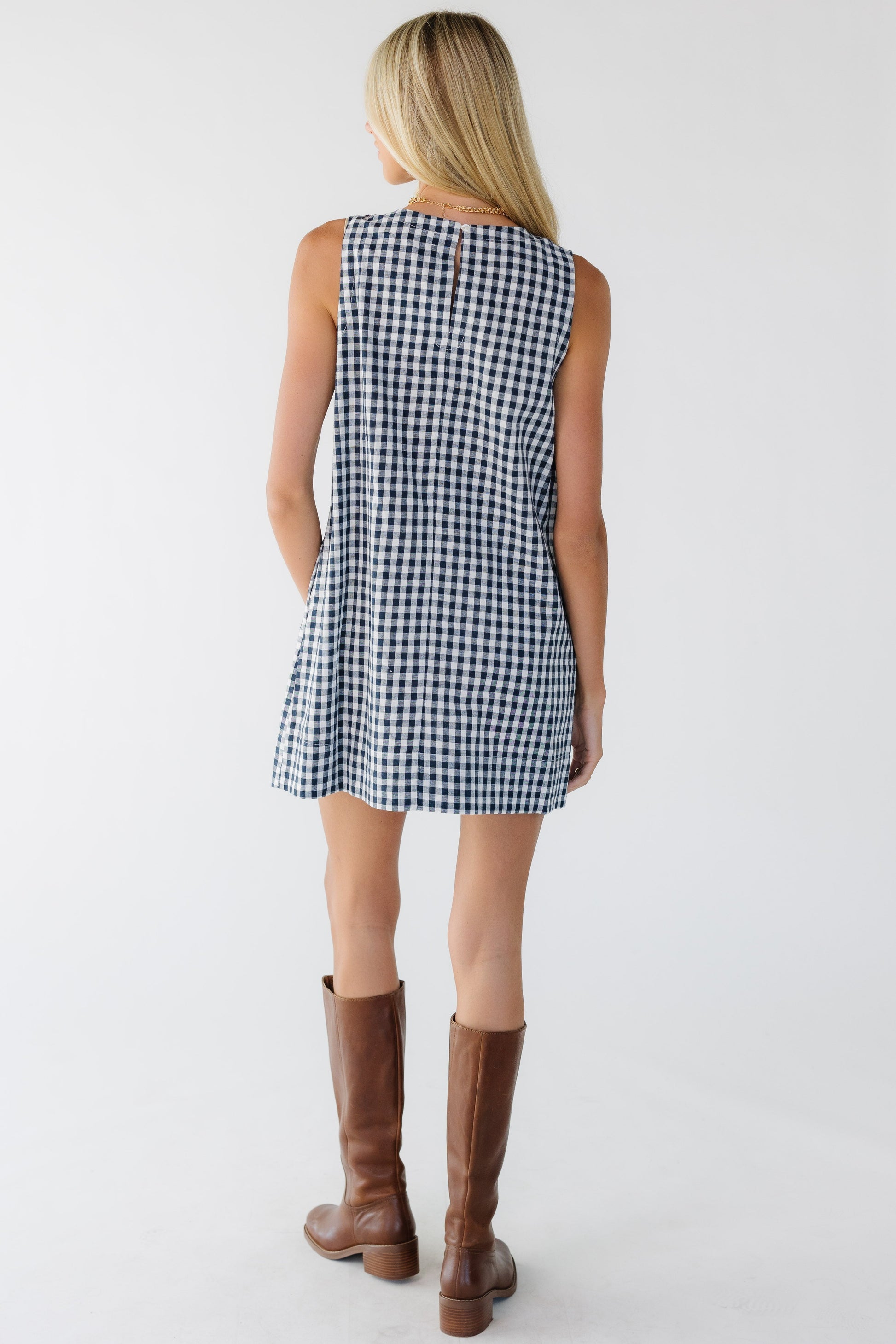 Back view of a woman wearing a shorts navy and white gingham loose fitting sleeveless dress.