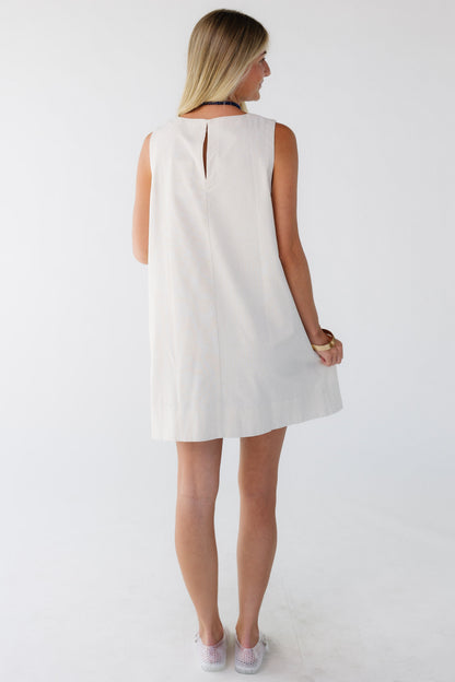 Back view of a woman wearing a cream loose fitting sleeveless shift dress.
