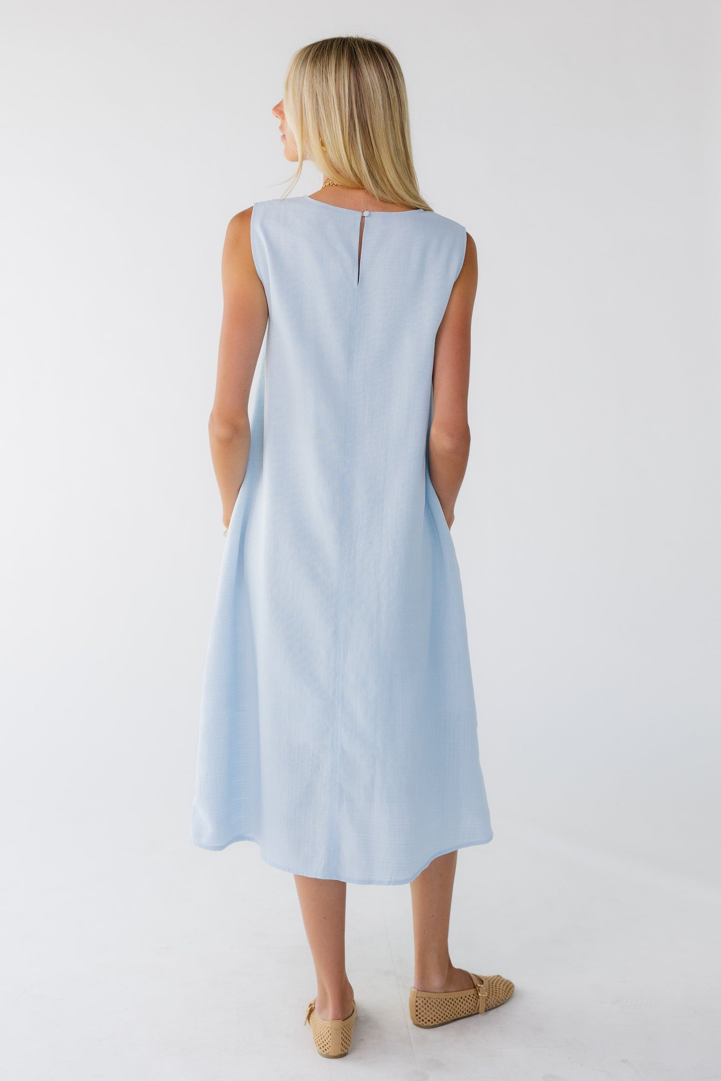 Back view of a woman wearing a loose fitting sleeveless shift dress in midi length.