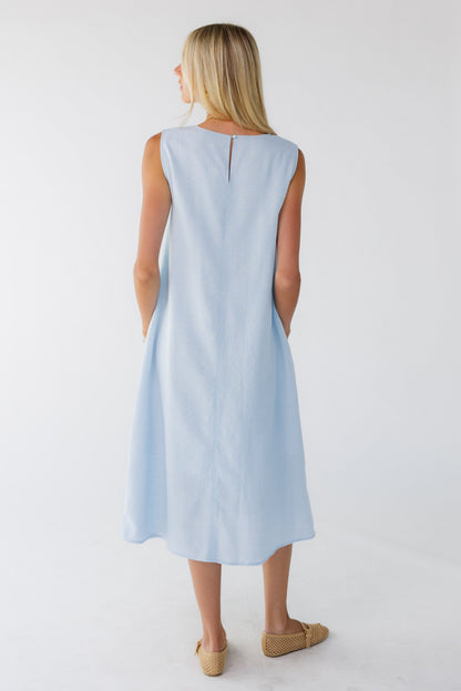 Back view of a woman wearing a loose fitting sleeveless shift dress in midi length.