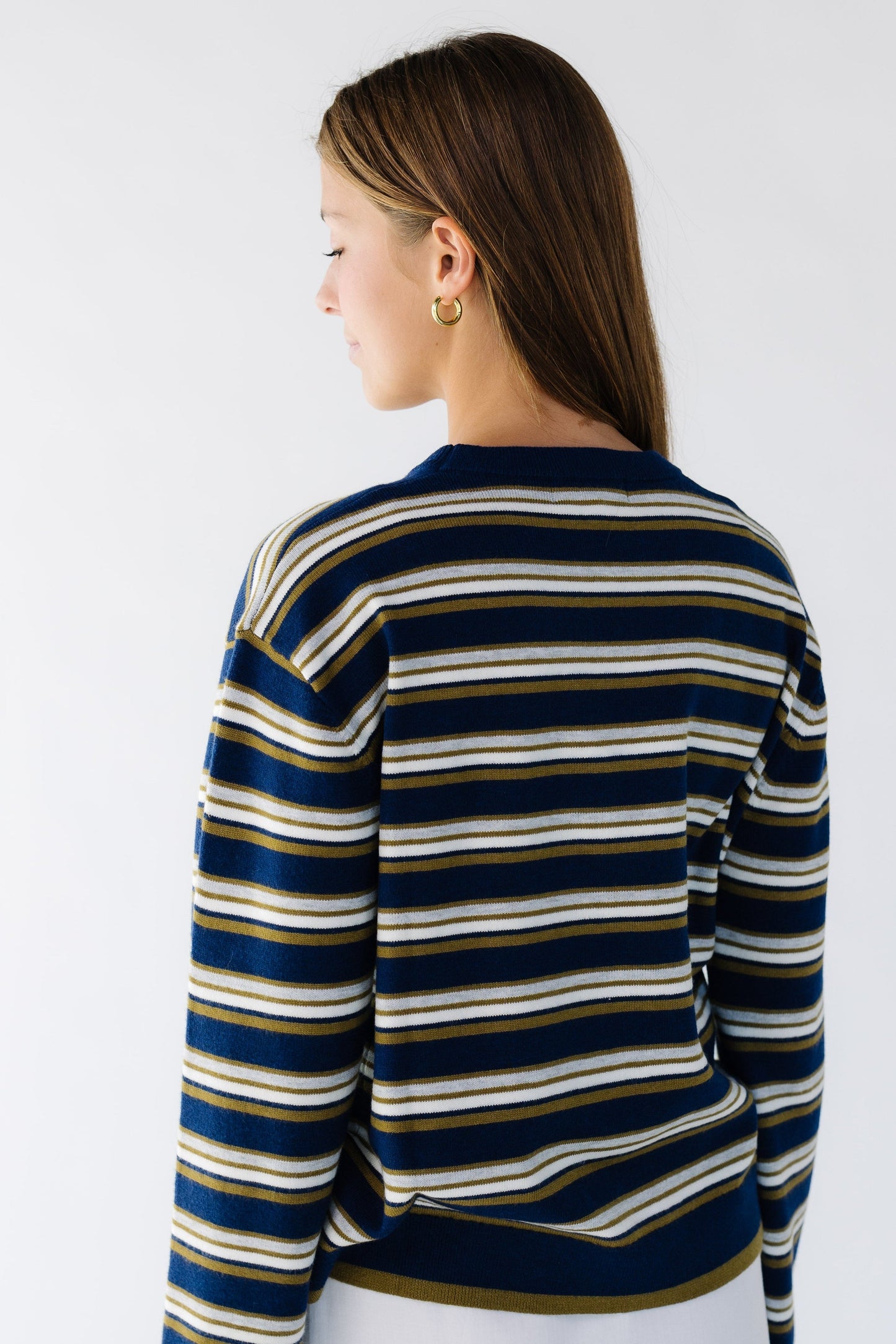 Back view of a woman searing a navy & multi-color stripe loose fitting sweater.
