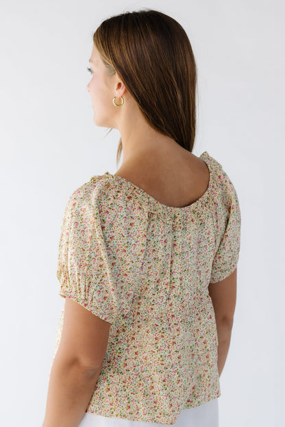 Back view of a woman wearing a yellow floral top with short puff sleeves and a round ruffled neckline.