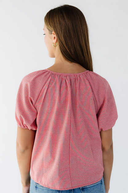 Back view of a woman wearing a loose fitting red gingham blouse  with short puff sleeves. 