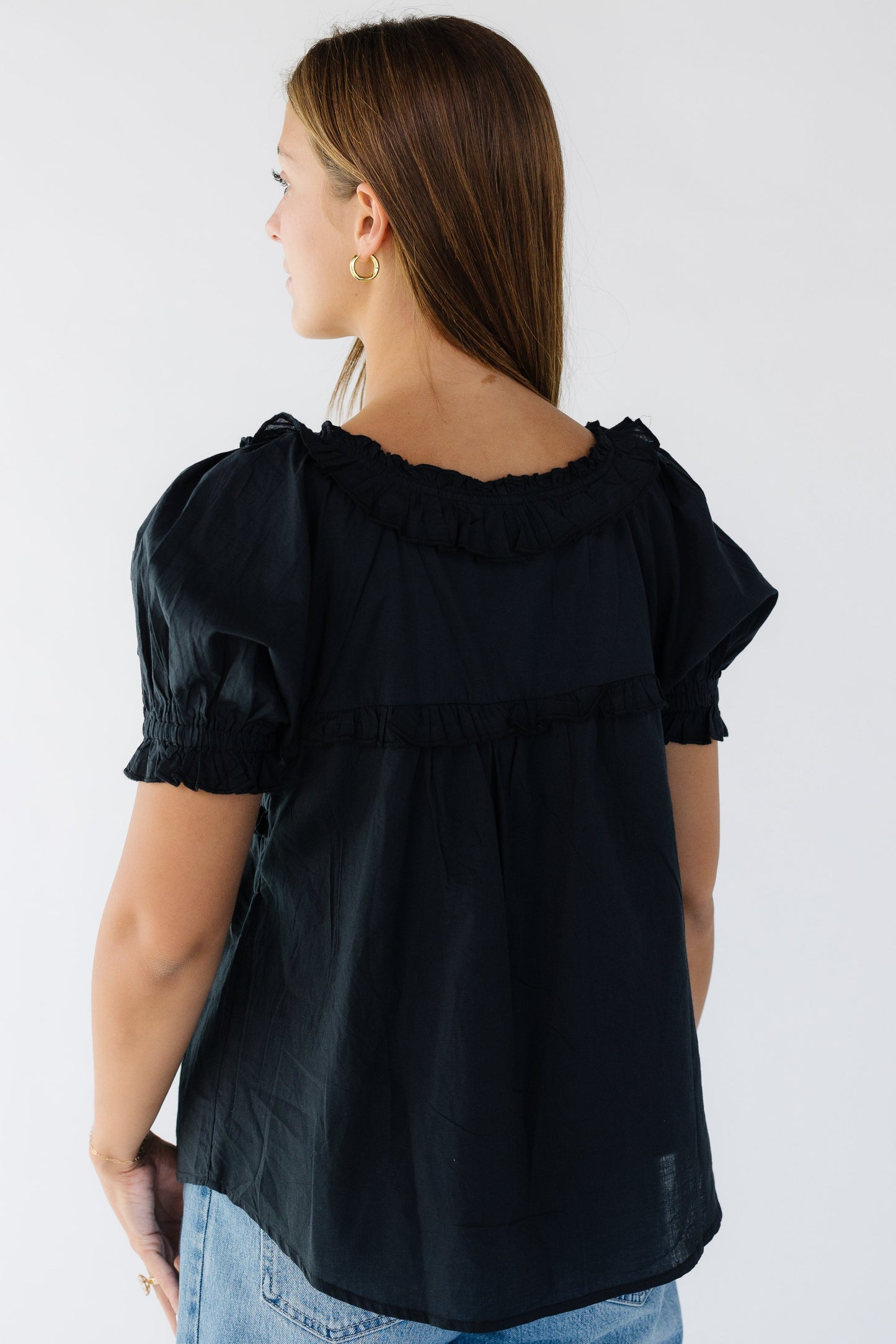 Back view of a woman wearing a black flowy blouse with short puff sleeves and a ruffled neckline.