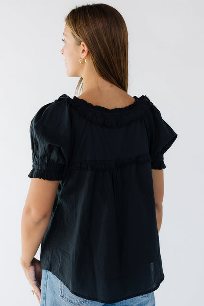 Back view of a woman wearing a black flowy blouse with short puff sleeves and a ruffled neckline.