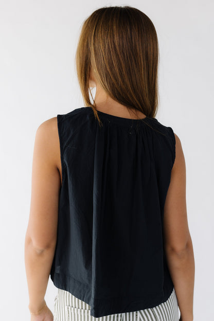 Back view of a woman wearing a black loose fitting sleeveless blouse.
