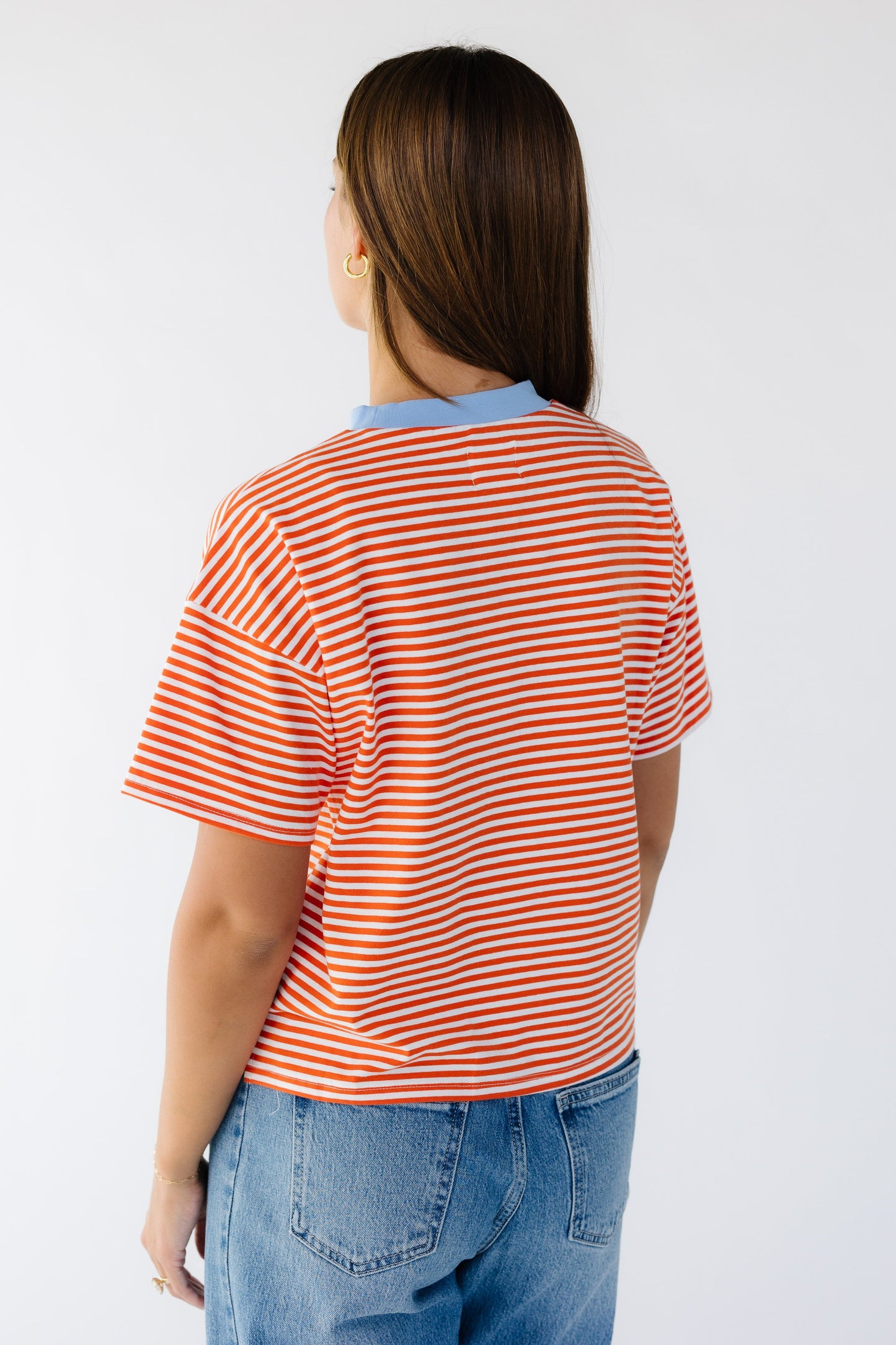 Back view of a woman wearing an orange and white stripe boxy tee with a contrasting blue crew neckline.