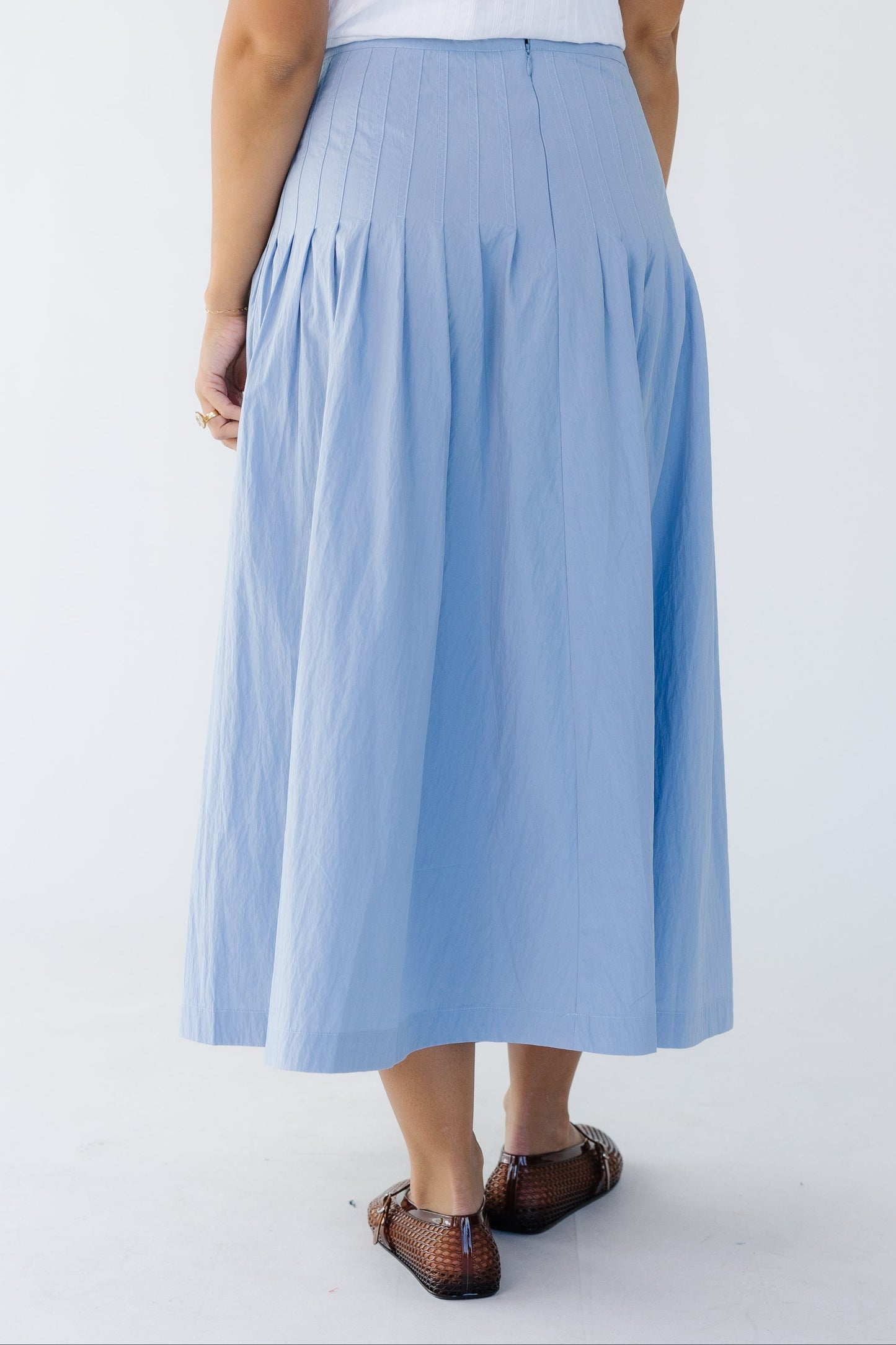 Back view of a woman wearing a blue midi skirt with sewn down pleats all around the hip.