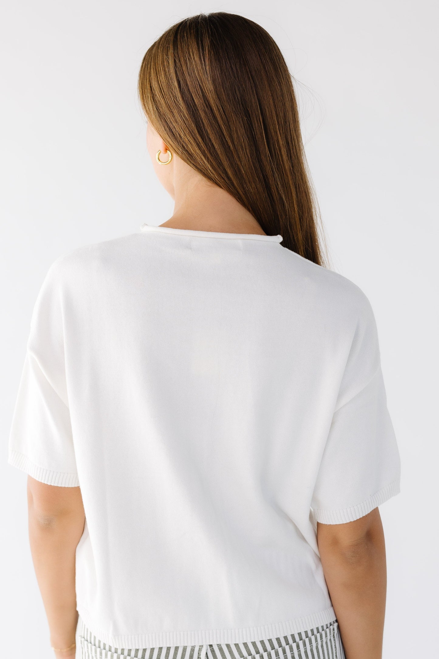 Back view of a woman wearing an ivory button down cardigan with short sleeves.