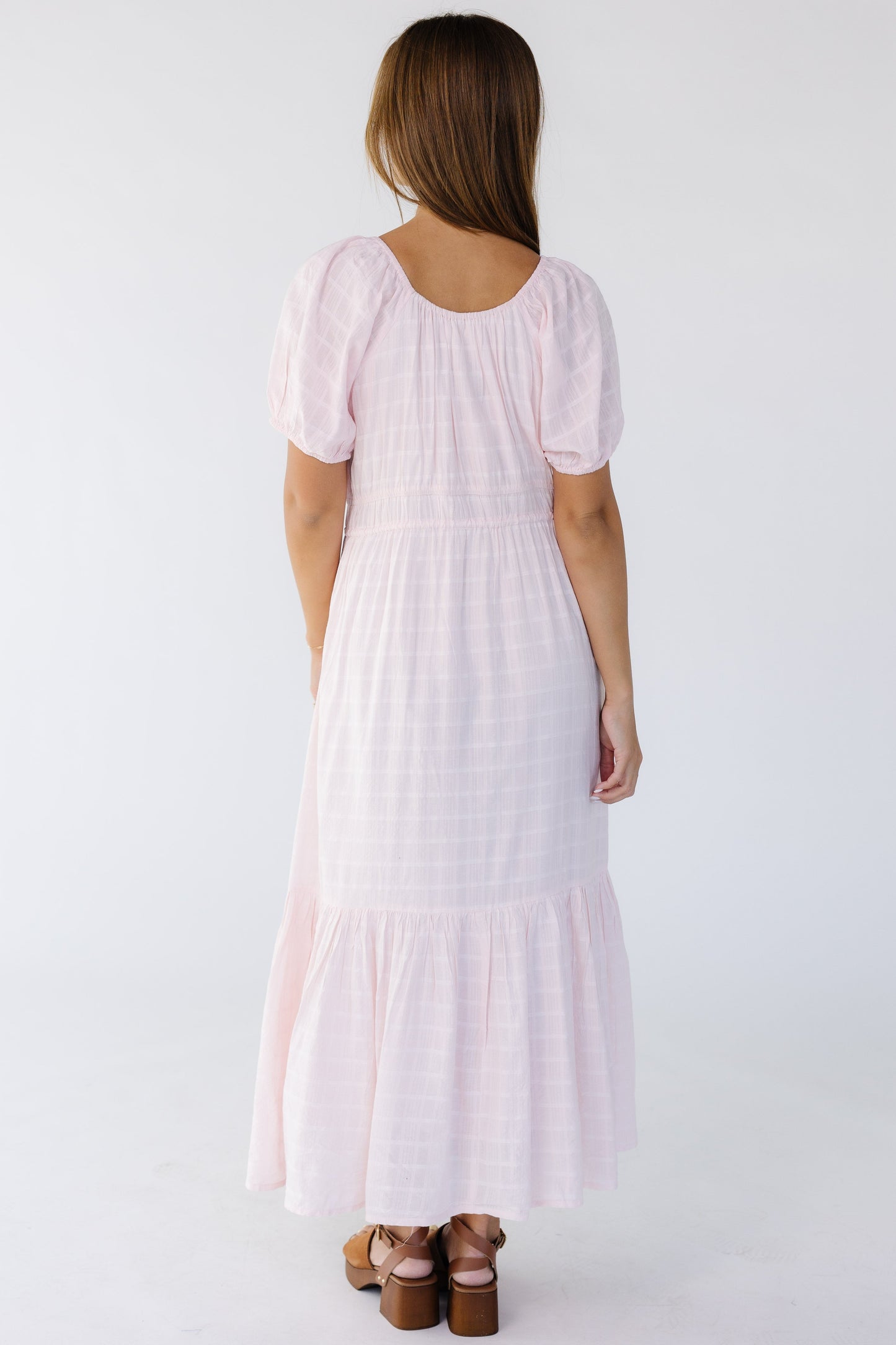 Back view of a young woman wearing a light pink midi-maxi dress with short puff sleeves.