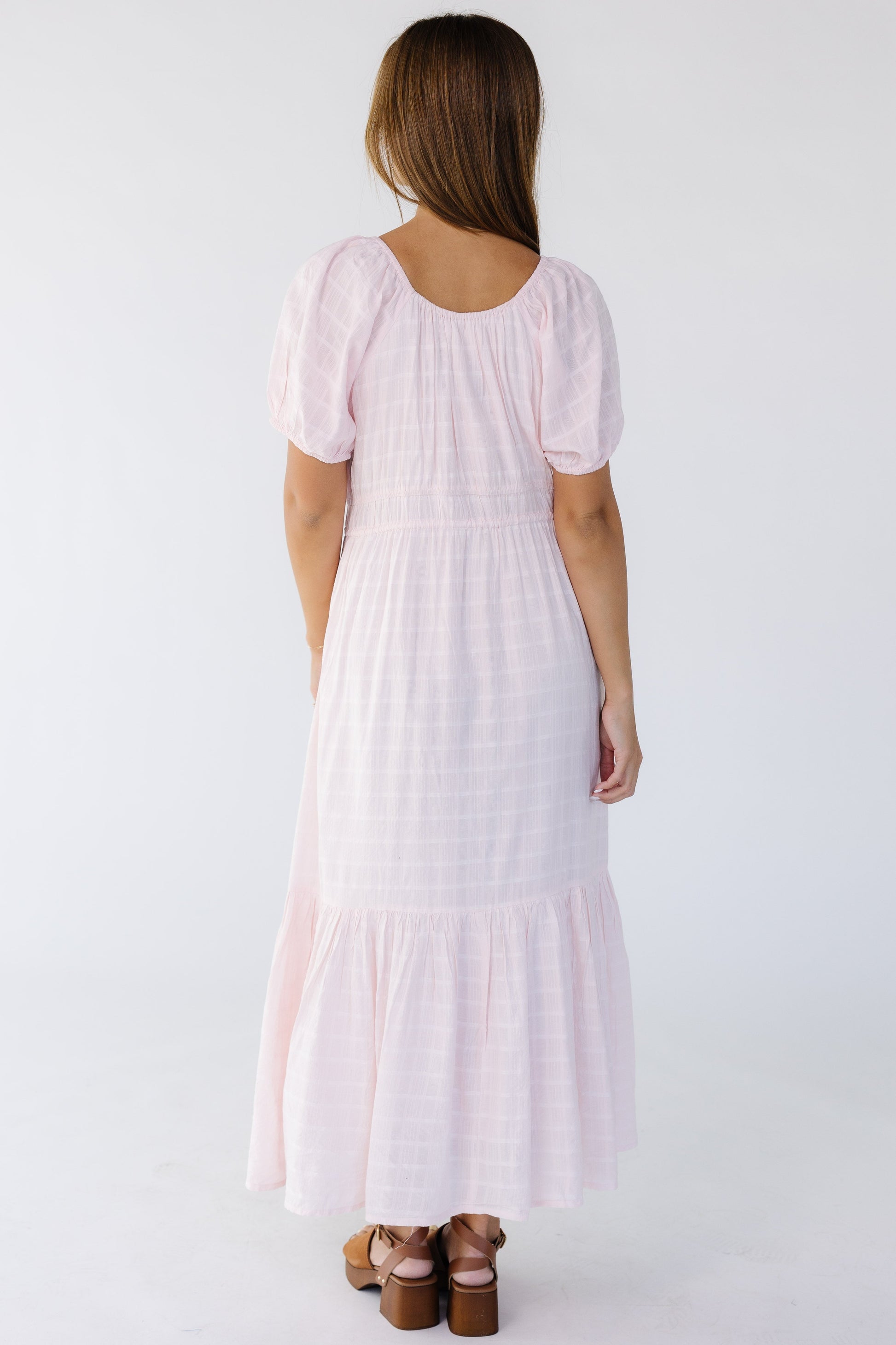 Back view of a young woman wearing a light pink midi-maxi dress with short puff sleeves.