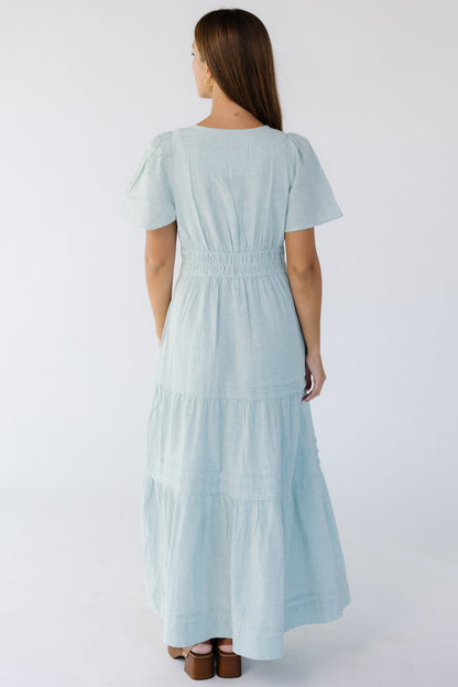 Back view of a woman wearing a green and white stripe tiered midi-maxi dress with short flutter sleeves, wide waistband.