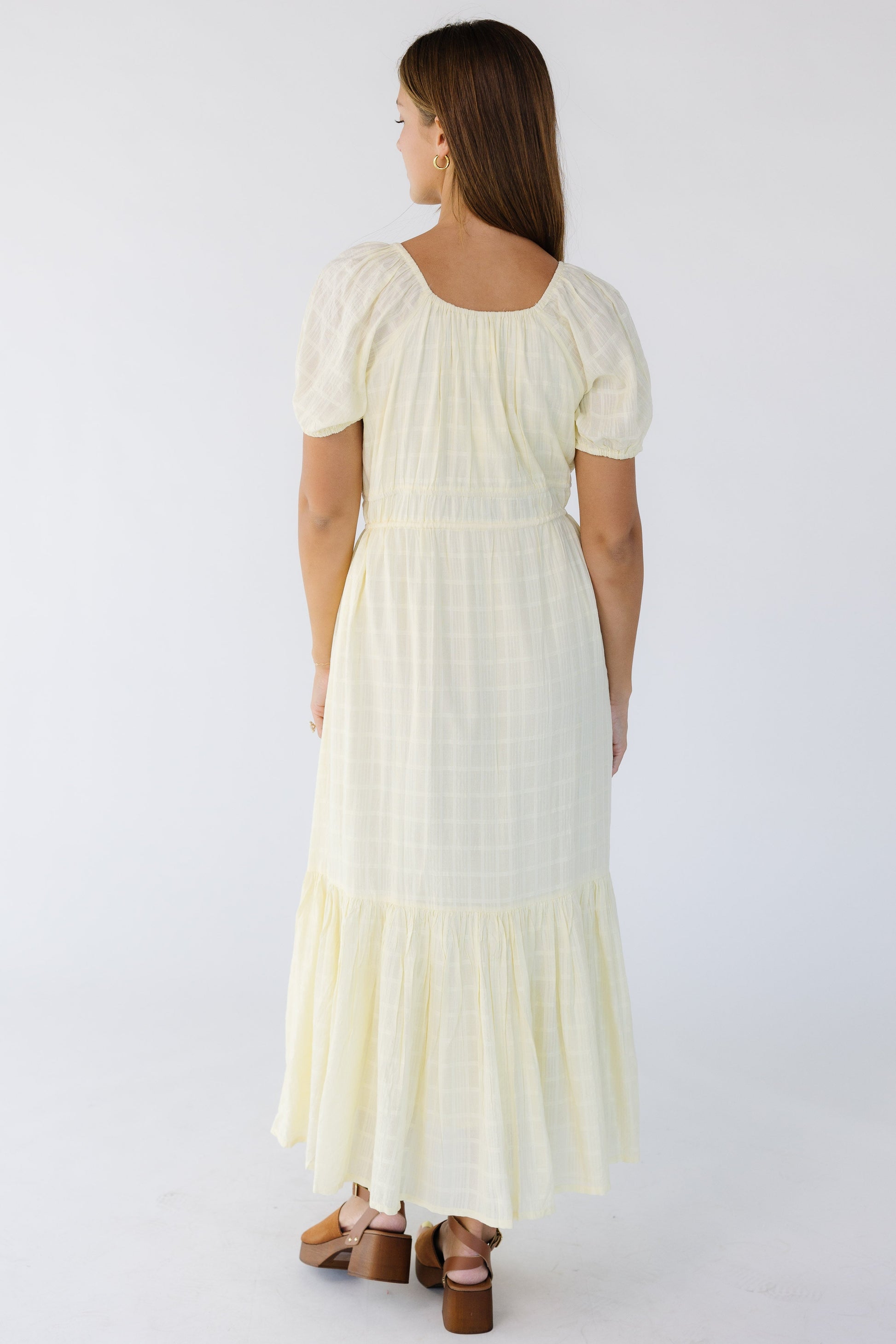 Back view of a young woman wearing a yellow midi-maxi dress with short puff sleeves.