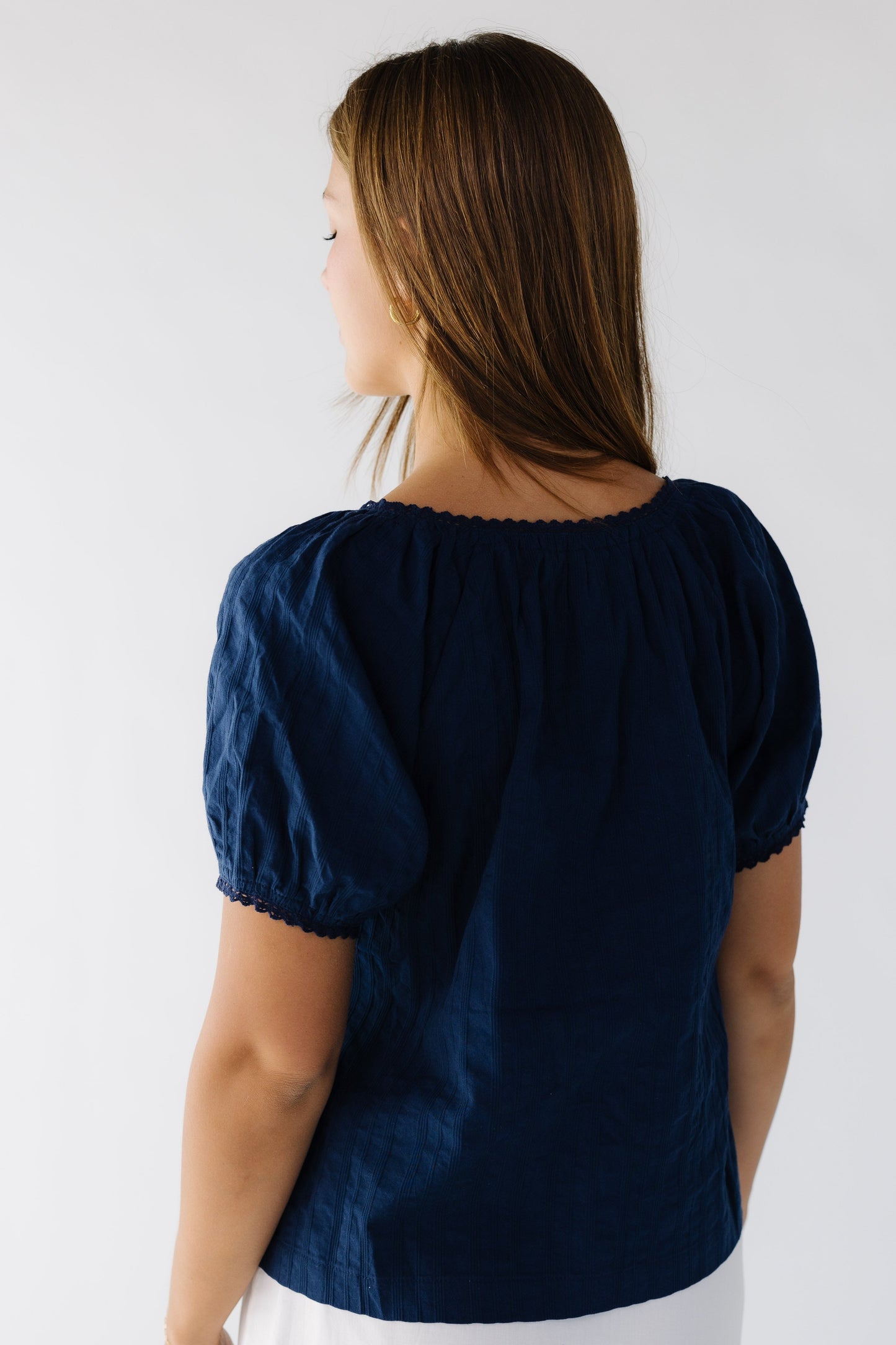 Back view of a woman wearing a navy loose fitting short sleeve blouse.
