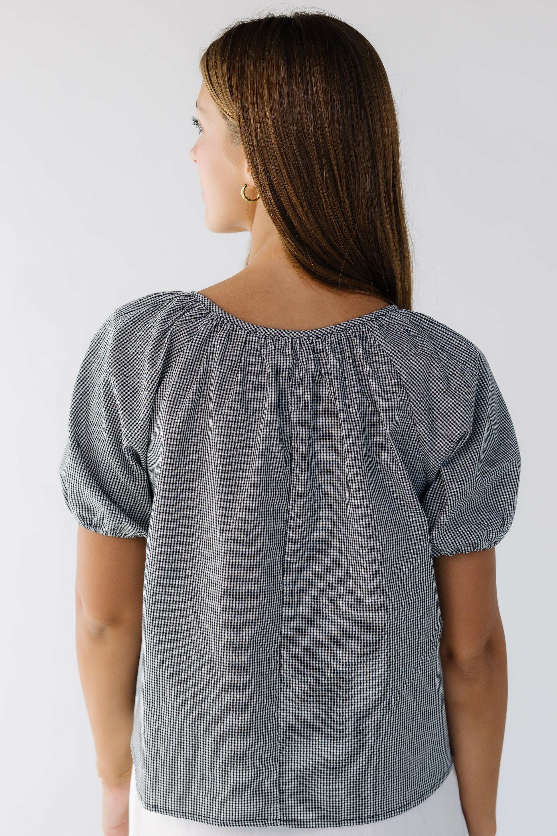 Back view of a woman wearing a loose fitting black gingham blouse with short puff sleeves.