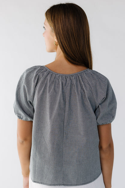 Back view of a woman wearing a loose fitting black gingham blouse with short puff sleeves.