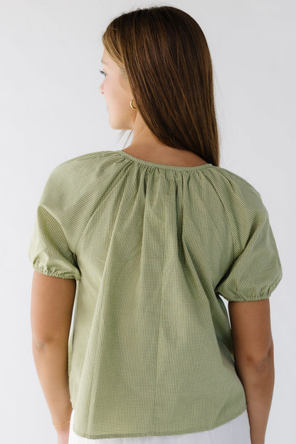 Back view of a woman wearing a green gingham loose fitting blouse with short puff sleeves.