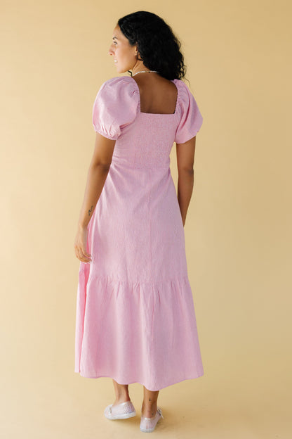 Back view of a woman wearing a red & white stripe midi-maxi dress with an elastic smocked back bodice panel, square back neckline large puff sleeves  and a wide bottom ruffle.