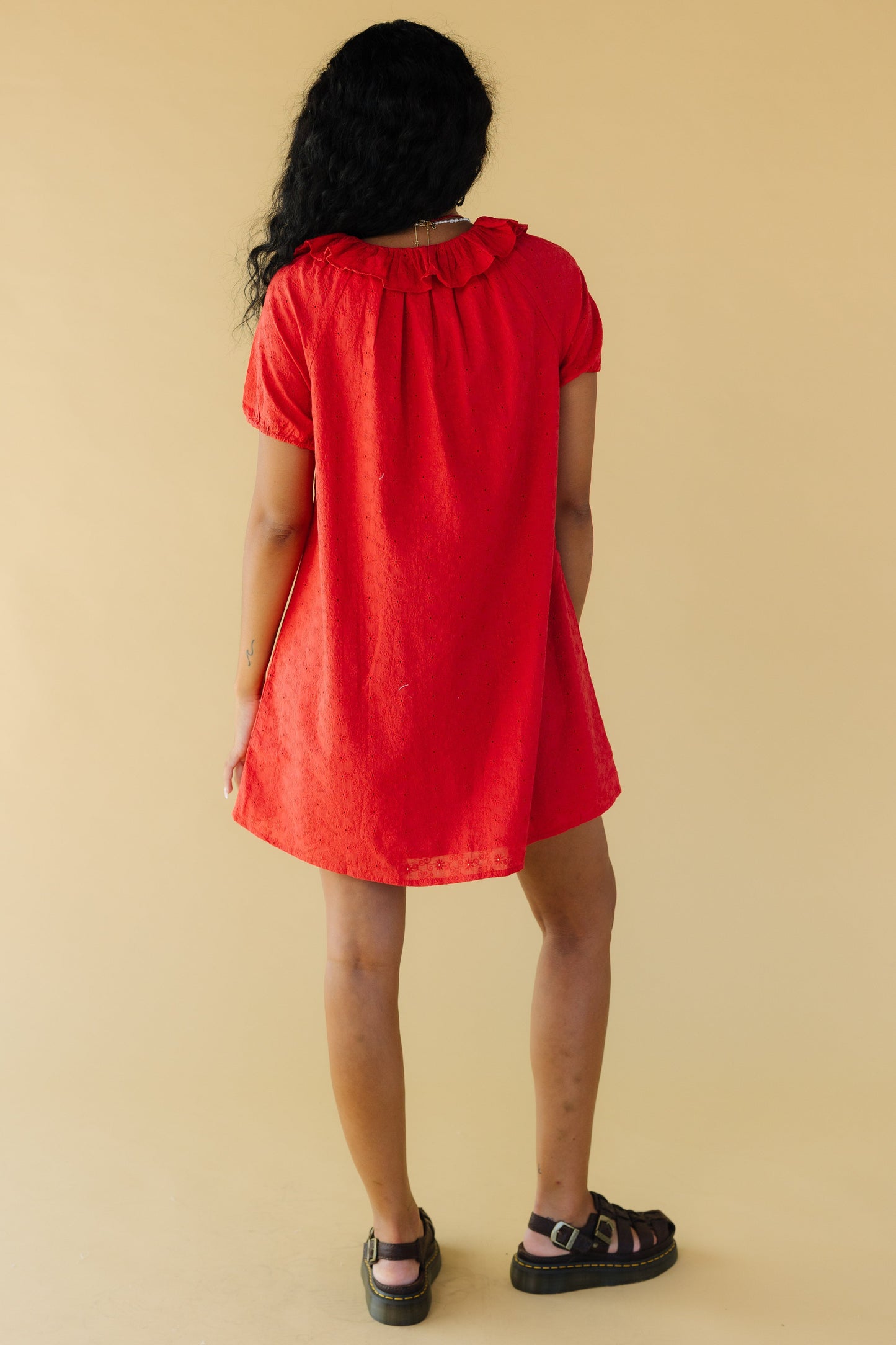 Back view of a woman wearing a short red eyelet dress with puff sleeves and a round ruffled collar.