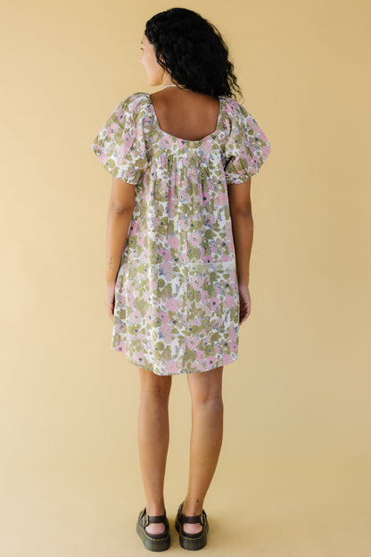 Back view of a young woman wearing a pink & green short dress with balloon sleeves and a square back neckline.