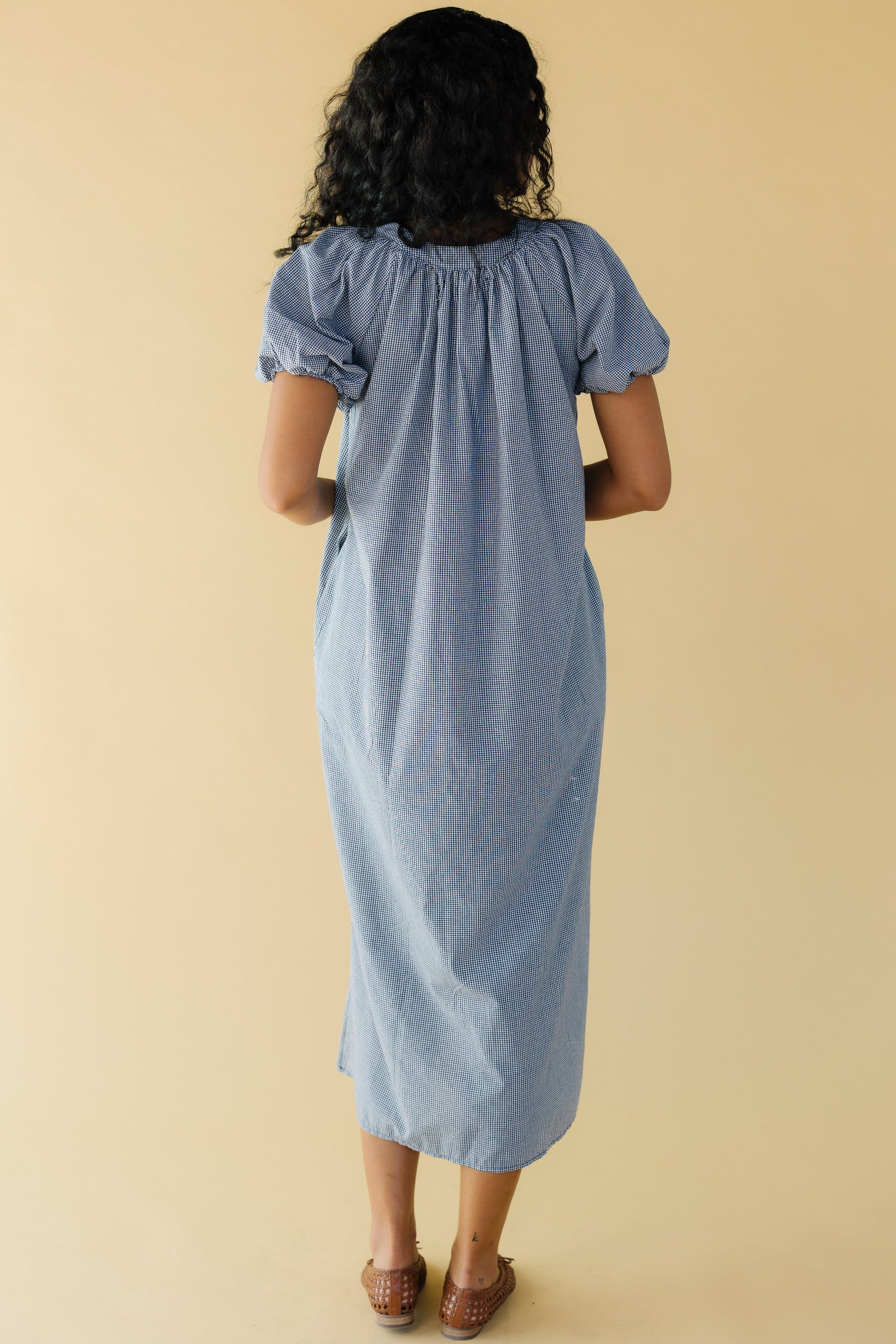 Back view of a woman wearing a navy & white gingham midi dress with balloon sleeves.
