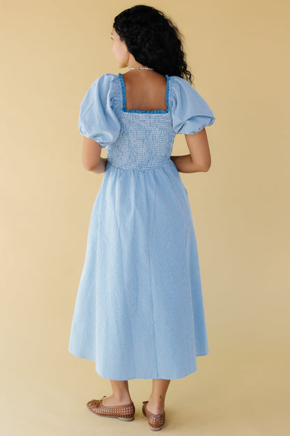 Back view of a young woman wearing a blue & white gingham midi dress with balloon sleeves and a lace trimmed square neckline.