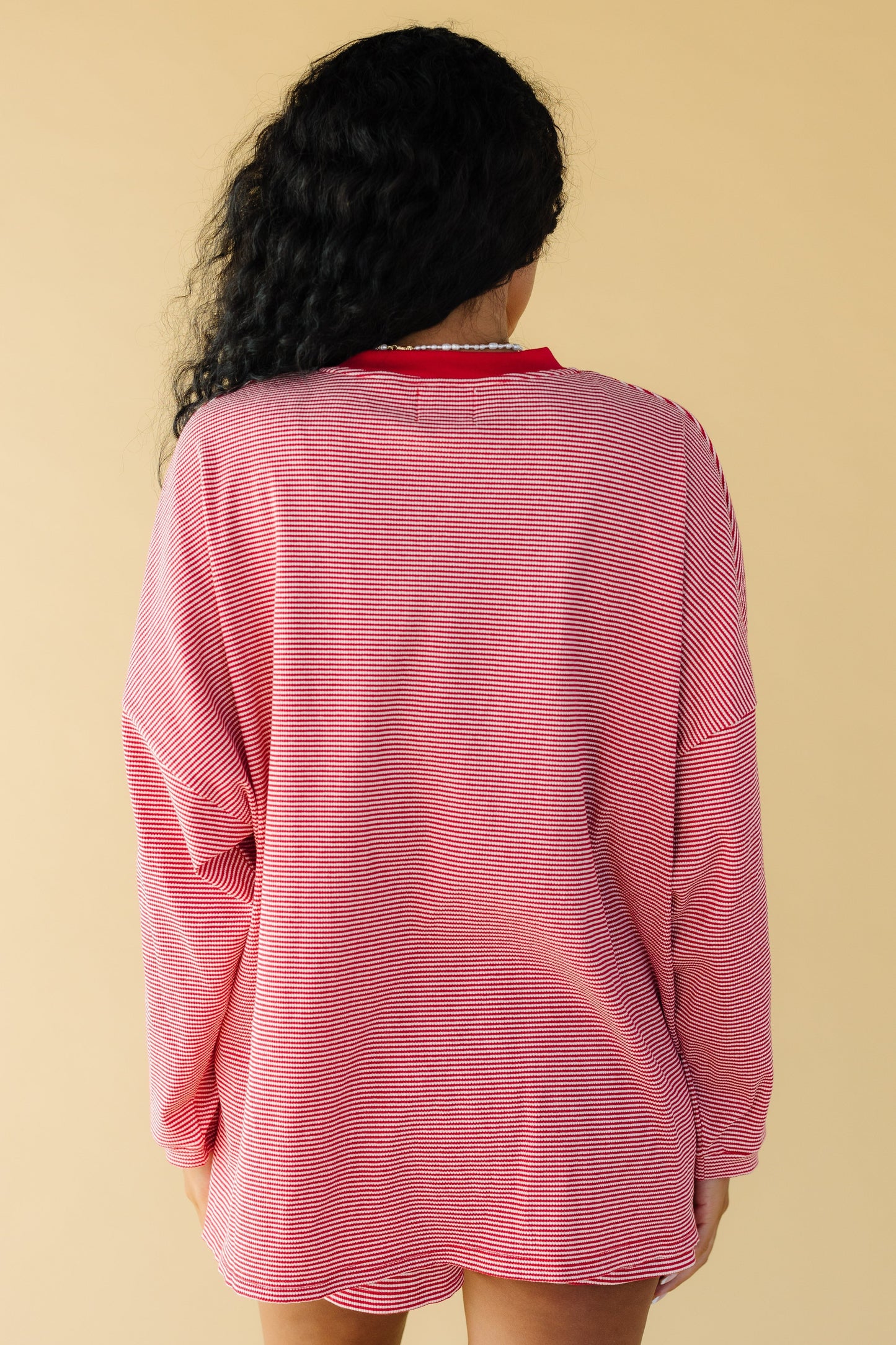 Back view of a woman wearing an oversized red & white stripe loose fitting top with long sleeves.