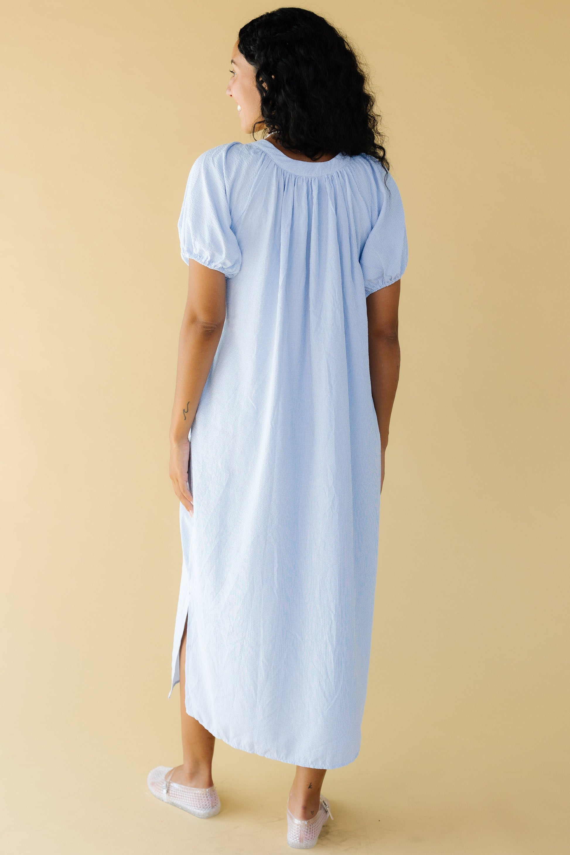 Back view of a woman wearing a light blue  plaid midi dress with side slits with large puff sleeves.
